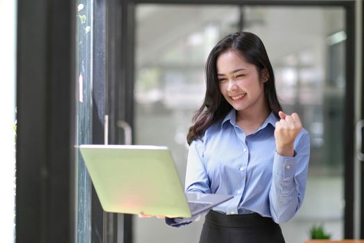 Happy Asian businesswoman holding laptop with celebrate success online marketing in the office.