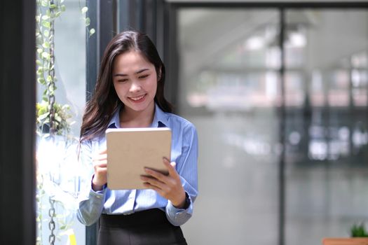 Beautiful businesswoman using stylus pen writing on tablet screen while standing in office room with copy space..