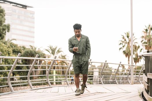 cool young african black man texting message on smartphone while walks in a park outdoors in the city, lifestyle and technology concept, copy space for text