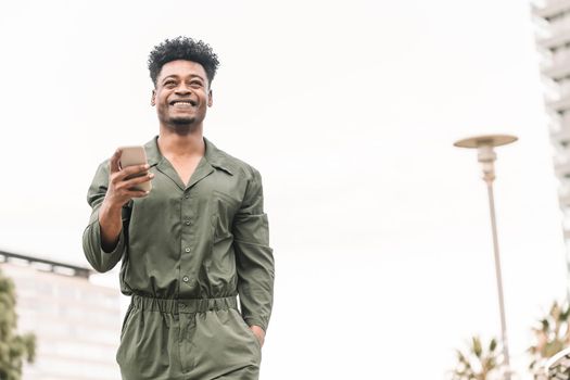attractive young african black man smiling and texting message on the phone while walks outdoors in the city, lifestyle and technology concept, copy space for text