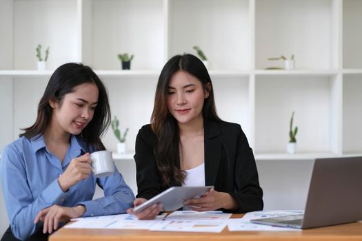 Two young Asian businesswoman discuss investment project working and planning strategy. Business people talking together with laptop computer at office..