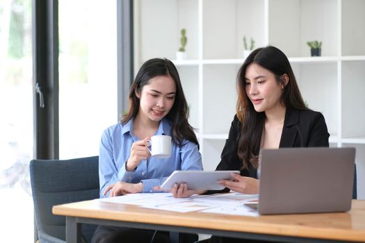 Two young Asian businesswoman discuss investment project working and planning strategy. Business people talking together with laptop computer at office..