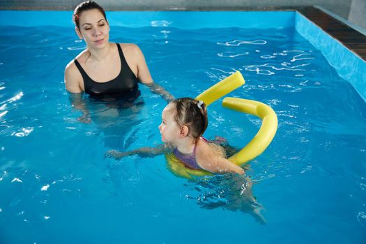 Preschool girl learning to swim in a pool with noodle