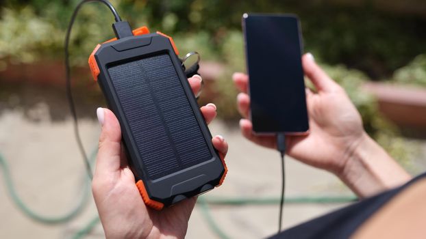 Female hand holding solar power bank and mobile phone closeup. Modern energy-saving devices concept