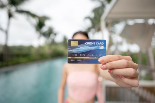 Woman holding credit card in hand by the pool, shopping online on vacation.