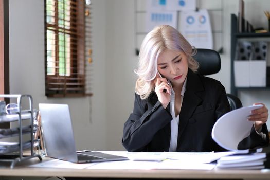businesswoman reading document while speaking on the phone at office.
