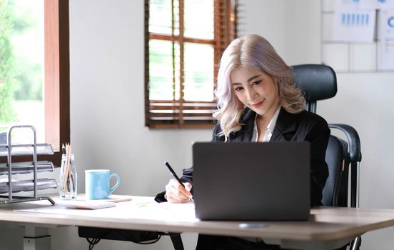 Beautiful young asian woman sitting at coffee shop using laptop. Happy young businesswoman sitting at table in cafe with tab top computer..