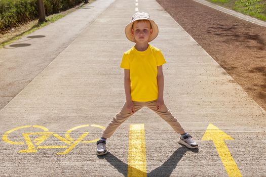 Little European boy in summer clothes and a summer hat, Panama. Blank t-shirt mockup for design, text, logo, template. Yellow T-shirt, place for drawing. The child stands on the road with arrows