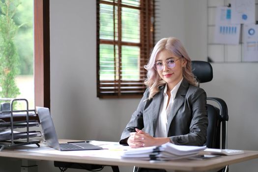 Charming young Asian woman wearing glasses holding a pen notebook laptop at the office. Looking at the camera..