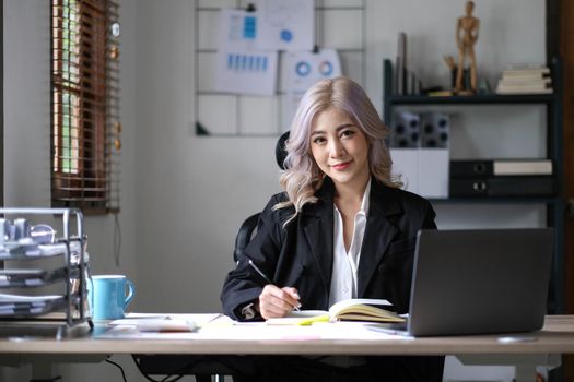 Charming Asian woman working at the office using a laptop Looking at the camera..