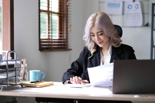 Beautiful Asian businesswoman analyzes charts using laptop calculator at the office..