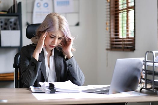 Asian businesswoman are serious at work causing headache stressed out with documents with a laptop at the office..