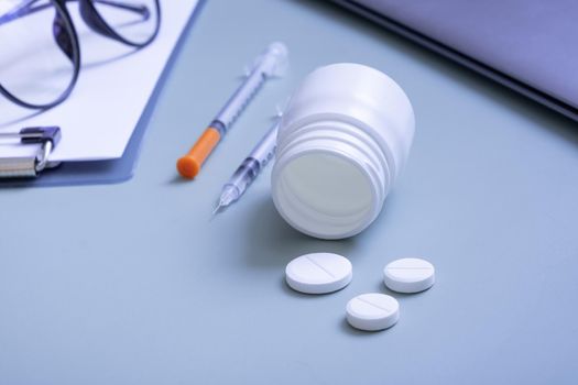 Pills with a container and syringes on the desktop on the background of a laptop and a tablet.