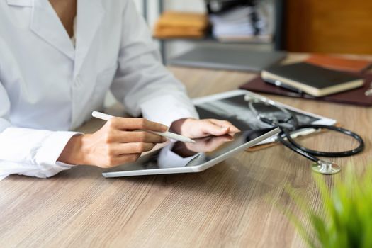 Cropped of female doctor using gadgets at workplace, holding smartphone and digital tablet. Unrecognizable therapist having online conversation with her patients, using mobile phone, closeup.