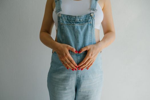 Pregnant girl in denim overalls. Hands on the stomach are folded in the shape of a heart. Great time to have a baby. Future mom.