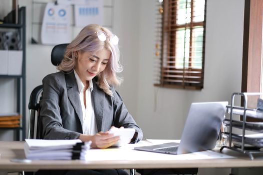 Young Asian businesswoman using a calculator to calculate business principles. Accounting statistics concept at the office..