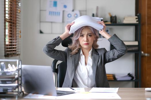 Portrait of beautiful asian woman at the desk with paperwork on her head. business overwhelmed stressed concept..