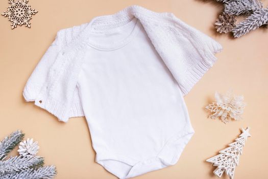 White baby bodysuit with sweater mockup for logo, text or design on beige background with winter decotations top view.