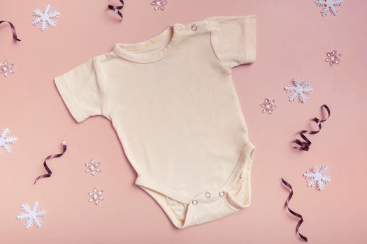 Yellow baby bodysuit mockup for logo, text or design on pink background with winter decotations top view.
