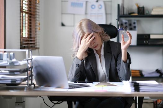 Image of an Asian woman who is tired and overthinking from working with a tablet at the office..