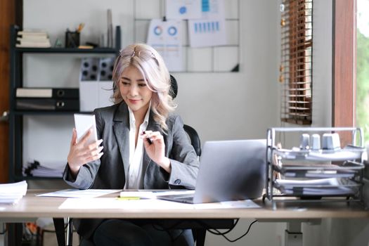 Happy young Asian business woman with a smile using smartphone at the office..