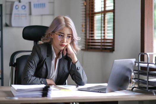 Tired business asian woman holds her fingers on her temples at work table. Irregular working day stressed worried, tired and overwhelmed concept.
