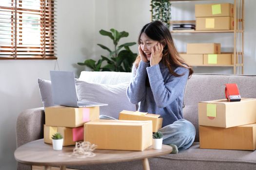 Happy young Asian woman entrepreneur, Smile for sales success after checking order from online shopping store in a smartphone at home office, Concept of merchant business online and eCommerce.