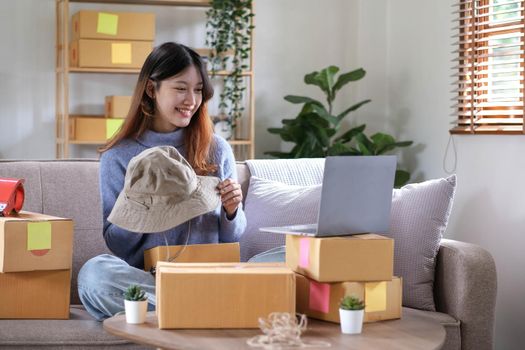 Startup small business entrepreneur SME, asian woman packing hat in box. Portrait young Asian small business owner home office, online sell marketing delivery, SME e-commerce telemarketing concept.