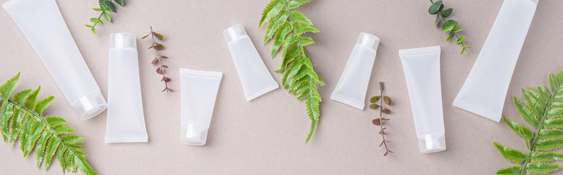 Set of skincare organic beauty product bottles and SPA cosmetic blank white matte containers with green plant leaves eucalyptus on gray clean background from above, flat lay mockup space for text