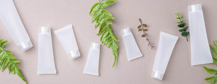 Set of skincare organic beauty product bottles and SPA cosmetic blank white matte containers with green plant leaves eucalyptus on gray clean background from above, flat lay mockup