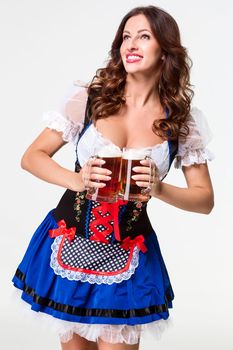 Beautiful young brunette girl in dirndl drinks out of oktoberfest beer stein. on white background.