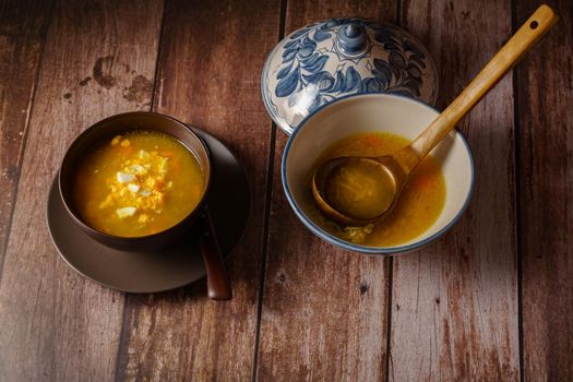 chicken noodle soup in a white soup tureen and a brown bowl with a plate and spoon on a wooden table