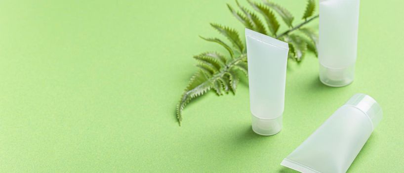 Set of skincare organic beauty product bottles and SPA natural cosmetic blank white matte containers with plant fern leaves on green clean background angle view, beaty cosmetics mockup copy space