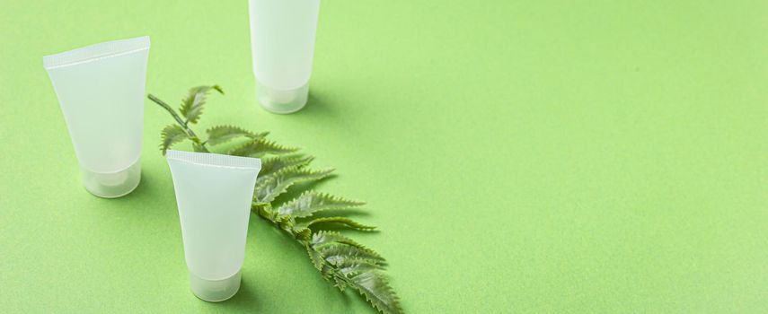 Set of skincare organic beauty product bottles and SPA natural cosmetic blank white matte containers with plant fern leaves on green clean background angle view, beaty cosmetics mockup copy space