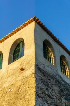 Building corner with green arched windows and tiled roof at sunset