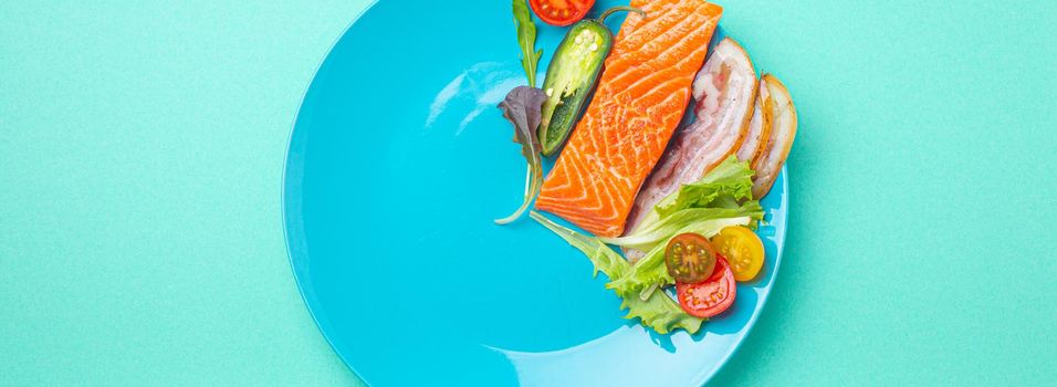 Intermittent fasting low carb hight fats diet concept flat lay, healthy food salmon fish, bacon meat, vegetables and salad on blue plate and blue background top view