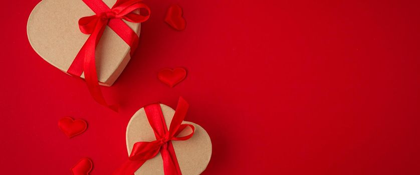 Two wrapped gift boxes in heart shape with red bow ribbon on red background and small padded hearts top view flat lay, presents for Saint Valentine day, love and relationship concept