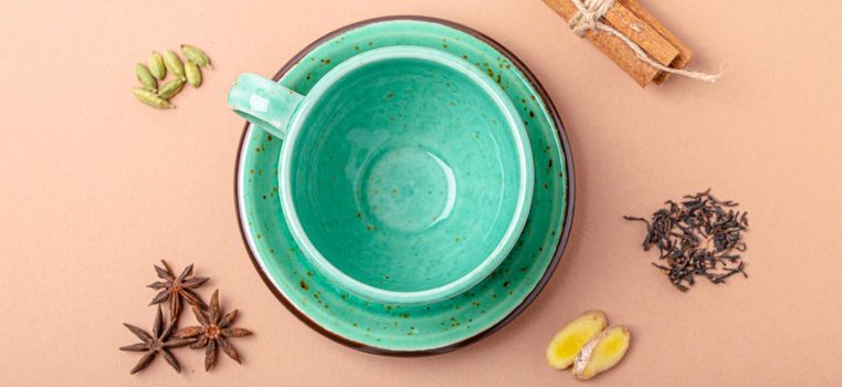 Empty rustic porcelain green teacup with saucer and spices ingredients for making healthy Indian tea drink masala chai from above on simple beige minimal background