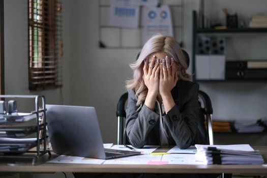 Tired and stressed young asian woman sitting at her working place...