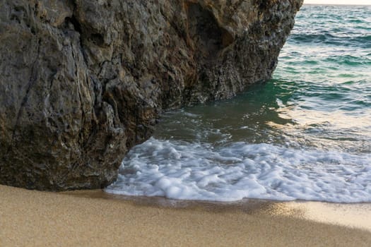 The foot of the cliff on the sandy shore, washed by the waves of the ocean close-up