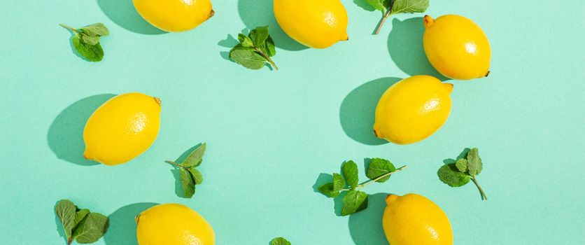 Fresh yellow lemons with mint on minimal blue background on bright sun light with hard shadows pattern summer background flat lay from above, citrus food composition, space for text