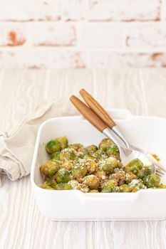 Healthy vegetarian dish roasted brussels sprouts with butter and parmesan cheese in white ceramic casserole close up on wooden table angle view, vegan food