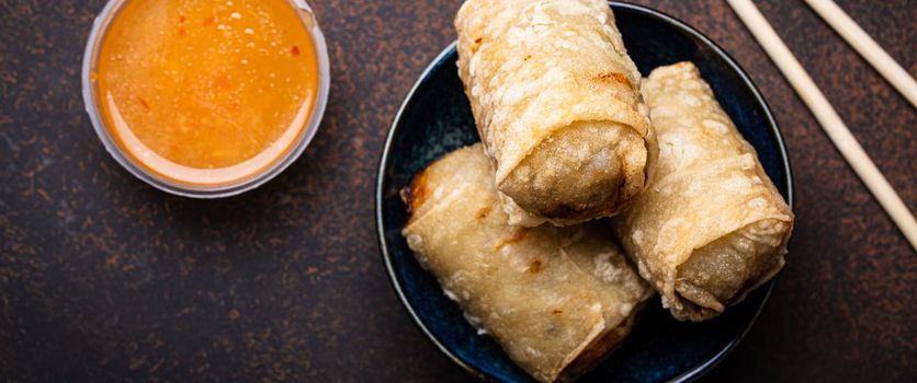 Chinese, Thai or Vietnamese traditional dish deep fried spring rolls with filling on plate with sweet sour sauce on rustic concrete background top view, Asian appetizer or snack with chopsticks