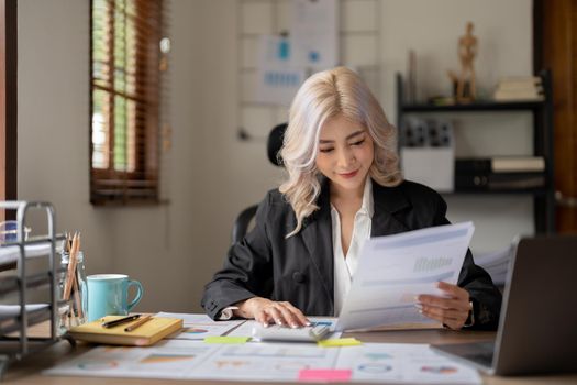 Happy smiling young asian entrepreneur woman counting profit, on calculator at laptop computer, analyzing benefits, enjoying financial success, job high result