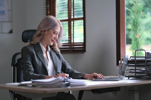 Charming businesswoman working on laptop at her workplace at modern office..