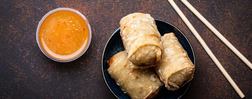Chinese, Thai or Vietnamese traditional dish deep fried spring rolls with filling on plate with sweet sour sauce on rustic concrete background top view, Asian appetizer or snack with chopsticks
