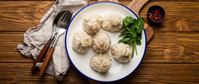 Khinkali, traditional dish of Georgian Caucasian cuisine, dumplings filled with ground meat on white plate with herbs on wooden rustic background table top view.