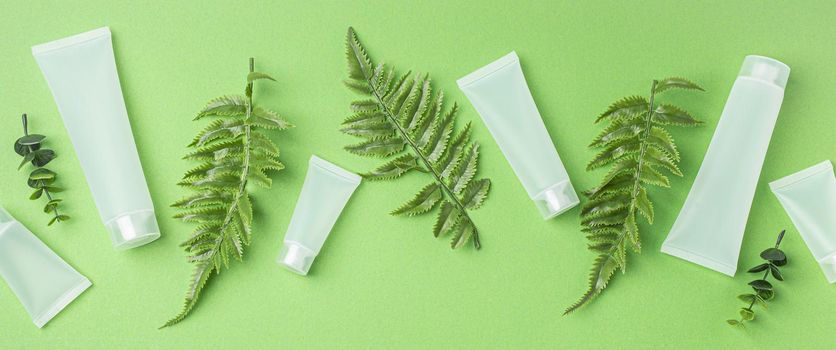 Set of skincare organic beauty product bottles and SPA cosmetic blank white matte containers with plant leaves eucalyptus on green clean background from above, flat lay mockup space for text