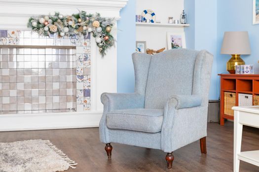 Wooden beige armchair stands next to fireplace. Vintage furniture. Cozy interior