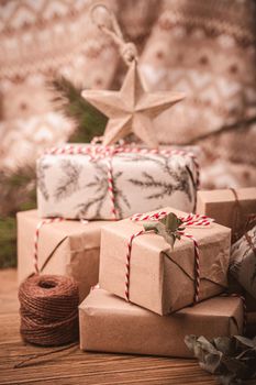 Pile of Christmas wrapped presents with twine string roll, fir tree branch, Christmas toy star at wooden background. Xmas decoration, cozy festive composition